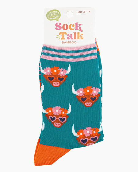  (Packaged Socks): A folded pair of Highland cow-themed socks inside their Sock Talk bamboo packaging, showcasing the cute cow design, floral details, and vibrant colours. The label states a UK 3-7 size range.
