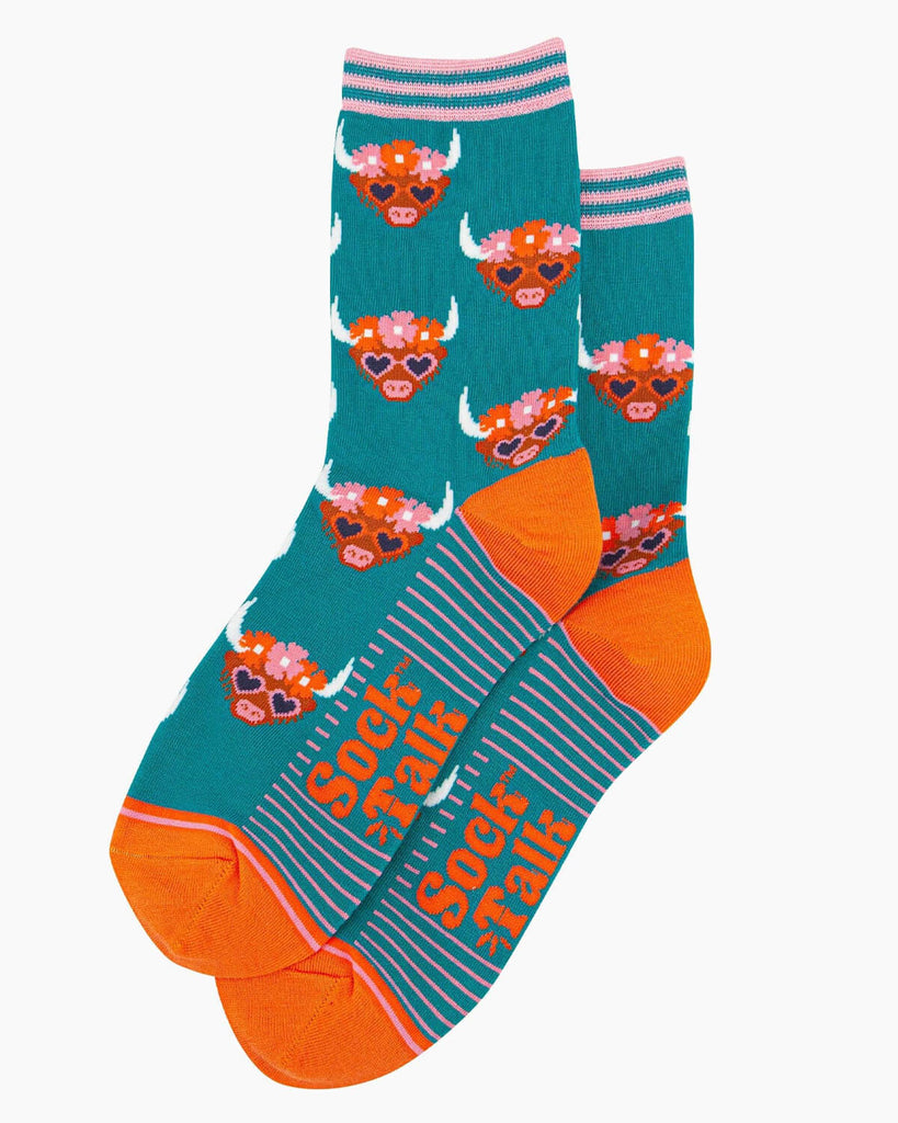  (Flat Lay of Socks): A pair of teal bamboo socks featuring a Highland cow with a floral crown and heart sunglasses. The socks have a striped cuff, an orange heel and toe, and the Sock Talk logo woven on the sole.