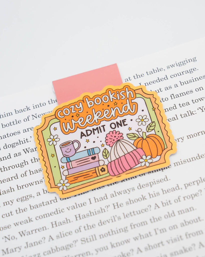 Magnetic bookmark clipped to an open book, shaped like a cute ticket stub and decorated with autumnal illustrations including a hot drink, stacked books, woolly hat, pumpkin, and flowers. Features the text “Cozy Bookish Weekend – Admit One.” A perfect reading companion for book lovers who adore cosy vibes and cute stationery. Sold by Rebel Romance, a small UK brand for quirky millennials.