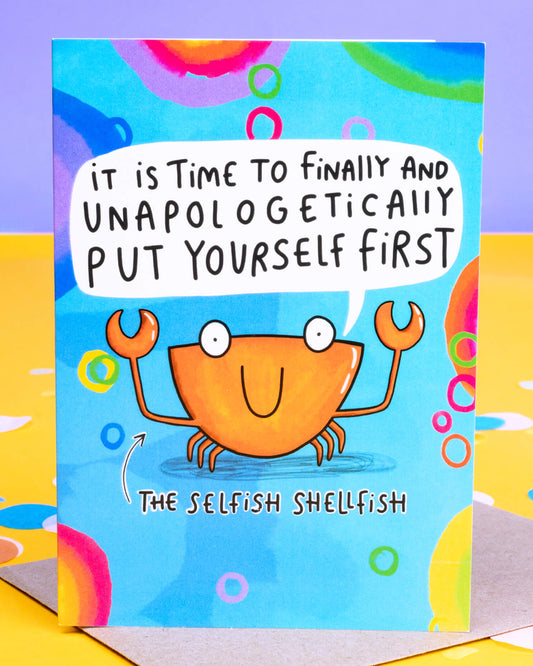 Bright and colourful A6 greeting card by Rebel Romance featuring The Selfish Shellfish by Katie Abey. The card shows a smiling orange crab on a blue background with rainbow bubbles, holding up claws beneath the message: “It is time to finally and unapologetically put yourself first.” A fun, motivational card designed to encourage self-care and self-love. Printed in the UK.