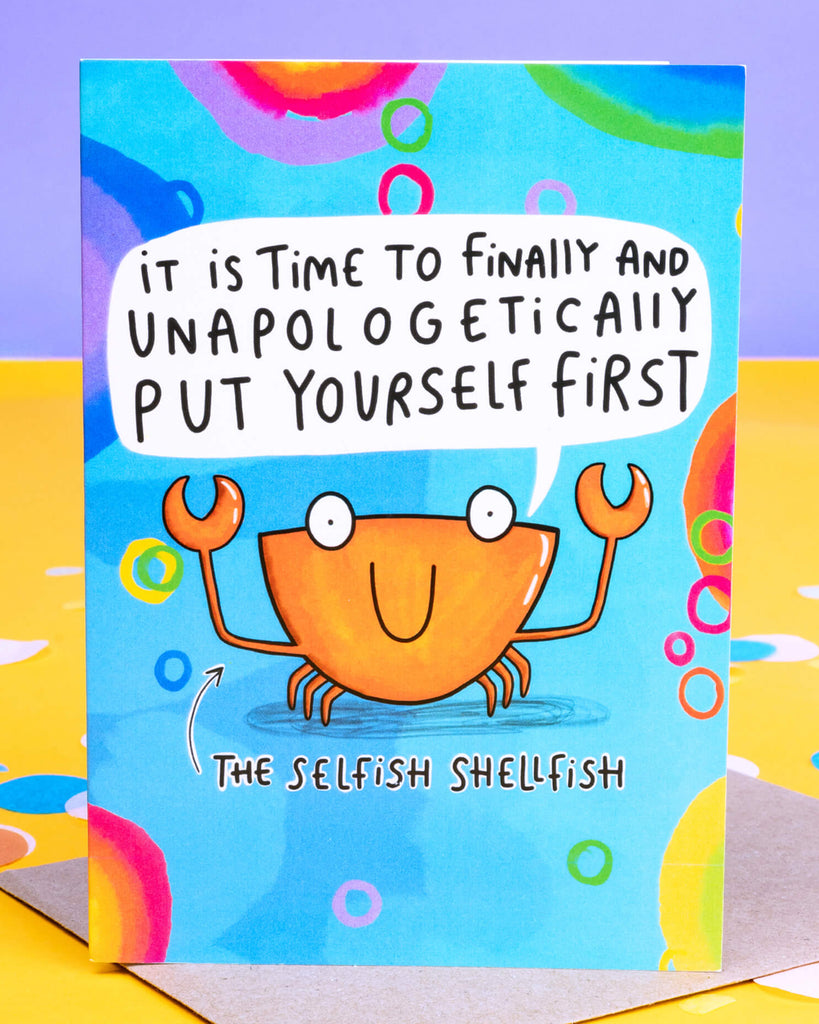 Bright and colourful A6 greeting card by Rebel Romance featuring The Selfish Shellfish by Katie Abey. The card shows a smiling orange crab on a blue background with rainbow bubbles, holding up claws beneath the message: “It is time to finally and unapologetically put yourself first.” A fun, motivational card designed to encourage self-care and self-love. Printed in the UK.