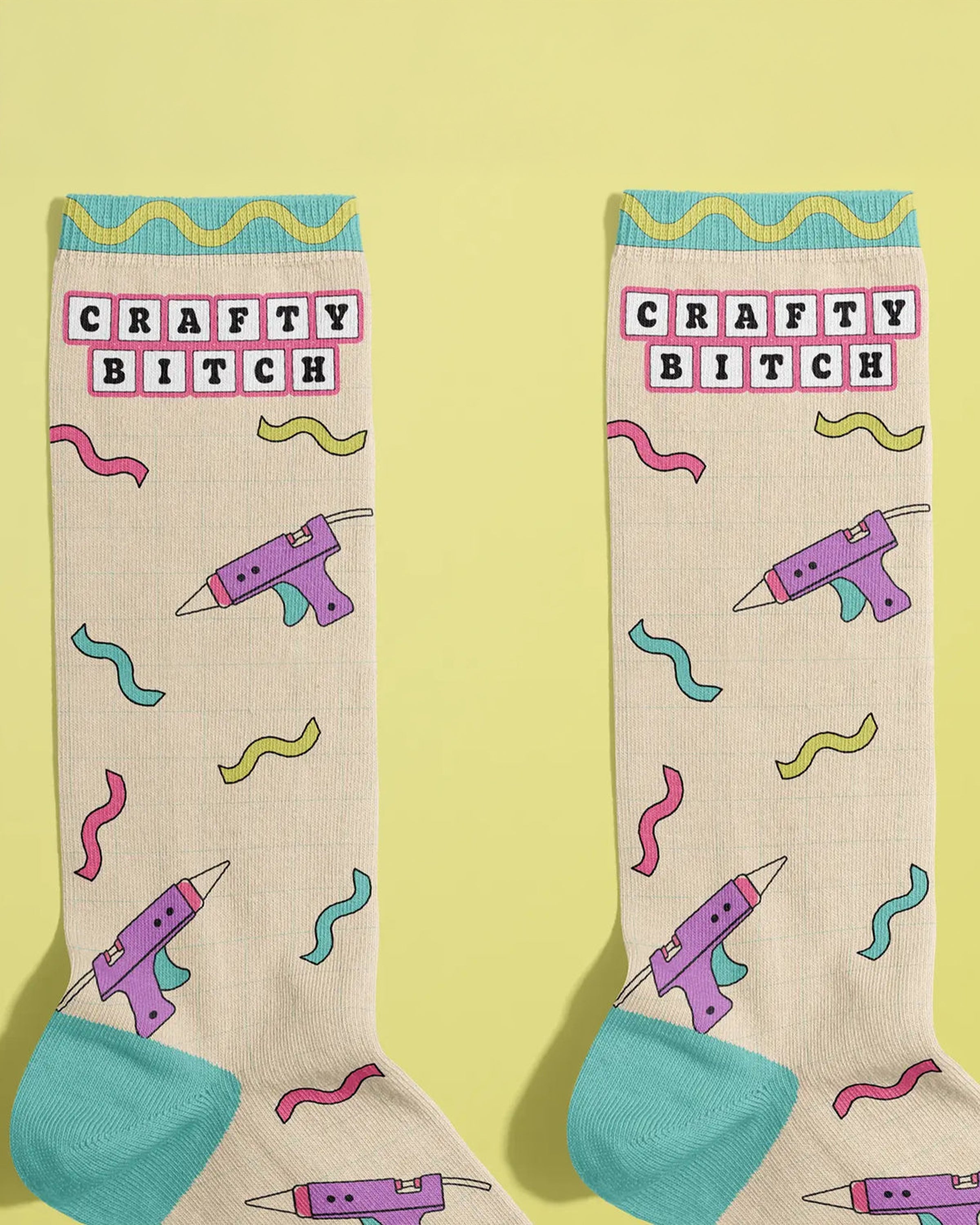 Pair of beige Rebel Romance crew socks by FUN CLUB displayed flat on a yellow background. The socks feature the phrase 