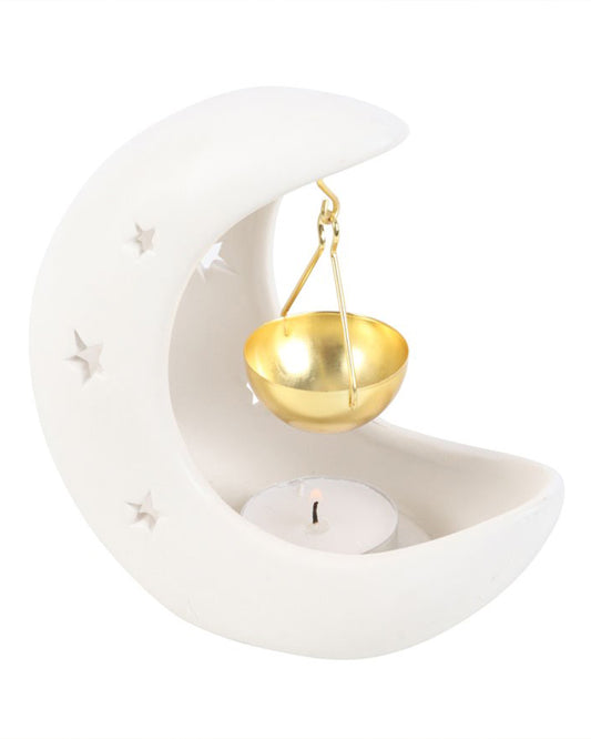 Close-up of the Rebel Romance crescent moon oil burner in white ceramic with star-shaped cut-outs and a glowing gold hanging bowl above a tealight. Mystical homeware gift idea for millennials.