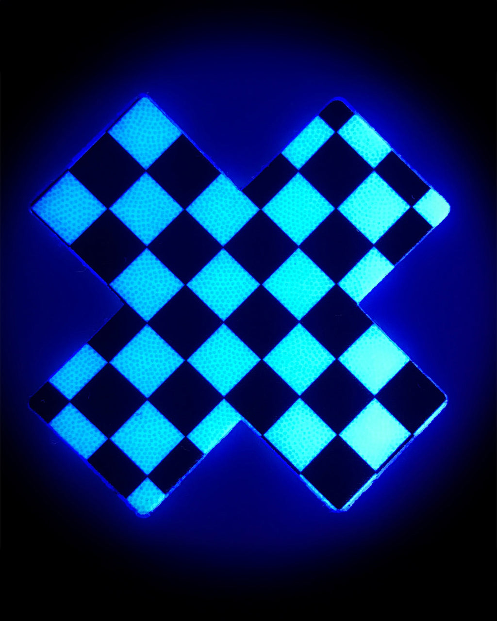 The Plus X: Black & White Checker Cross Nipple Pasties by Pastease shown glowing in the dark with a blue hue on a black background.