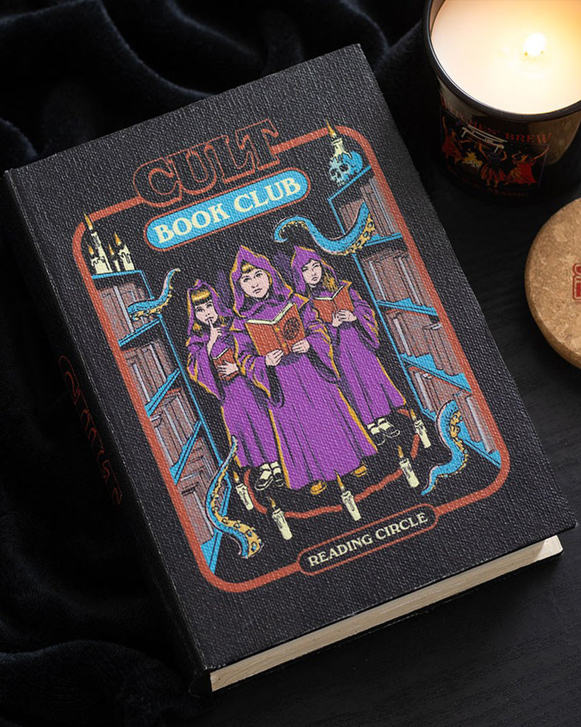 Styled photo of the Cult Book Club Book Shaped Storage Box by Steven Rhodes, surrounded by a candle and coaster. Available at Rebel Romance, this gothic book-style storage box is perfect for hiding trinkets, incense, or snacks. Fun alternative gift idea for millennials.