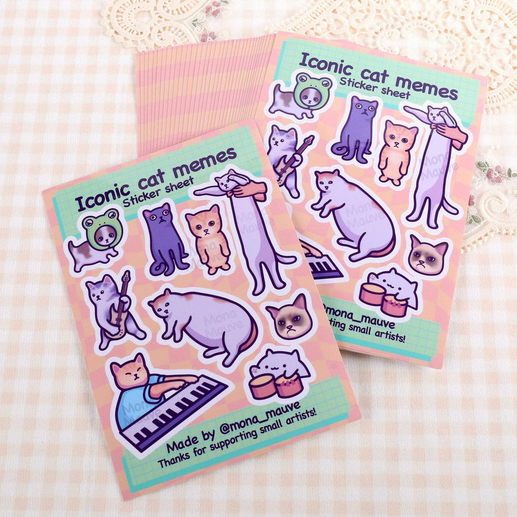 Two Iconic Cat Memes Sticker Sheets by Mona Mauve displayed on a soft, checkered fabric. Each sheet includes 9 playful vinyl stickers of internet-famous cats, perfect for decorating laptops, notebooks, or gifts. A fun design by a small indie artist, ideal for fans of funny feline content.