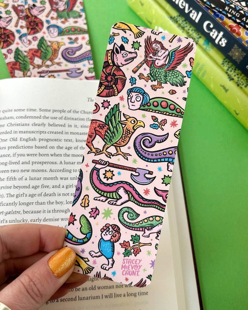The reverse side of a medieval creatures bookmark by Stacey McEvoy Caunt, filled with odd dragons, birds, faces, and axe-wielding critters, held by a hand with glittery orange nail polish. A Rebel Romance exclusive for lovers of the weird and wonderful.