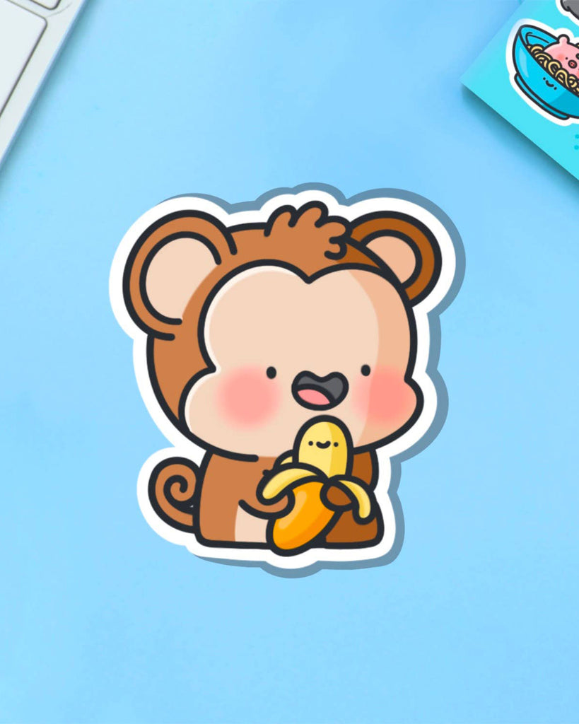 Toastedink monkey sticker hugging a cute banana on a pastel blue background. Sold by Rebel Romance, a UK brand known for quirky accessories and fun characters.