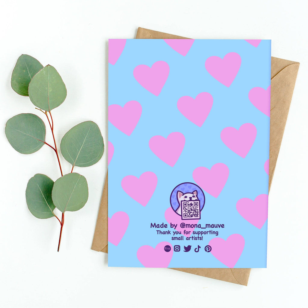 Back of the “Respect Pronouns” greeting card, designed by Mona Mauve for Rebel Romance. Features a blue background with pink hearts, a cartoon cat logo with QR code, and text reading “Made by @mona_mauve – Thank you for supporting small artists!” Shown with kraft envelope and eucalyptus leaves.