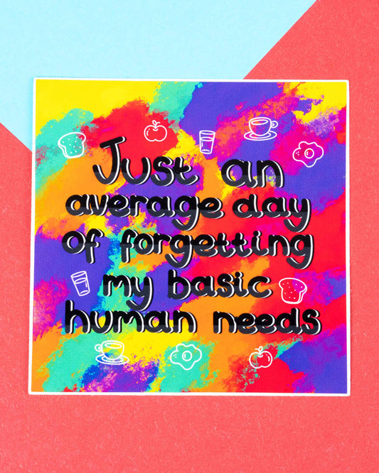 Square vinyl sticker with the phrase “Just an average day of forgetting my basic human needs” in playful black lettering, surrounded by doodles of food and drink. The sticker has a bold rainbow splatter background and is photographed on a red and blue geometric background. Sold by Rebel Romance, a UK brand celebrating alternative fashion and millennial-friendly gifts.