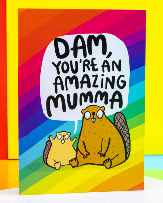 A colourful A6 greeting card by Rebel Romance, illustrated by Katie Abey, featuring two cute cartoon beavers with the pun message “Dam, You’re An Amazing Mumma” in bold black lettering. Set against a vibrant rainbow background, the cheerful design is perfect for Mother's Day, birthdays or to show appreciation. Ideal for quirky, alternative card lovers in the UK.
