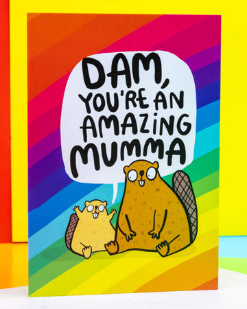 A colourful A6 greeting card by Rebel Romance, illustrated by Katie Abey, featuring two cute cartoon beavers with the pun message “Dam, You’re An Amazing Mumma” in bold black lettering. Set against a vibrant rainbow background, the cheerful design is perfect for Mother's Day, birthdays or to show appreciation. Ideal for quirky, alternative card lovers in the UK.