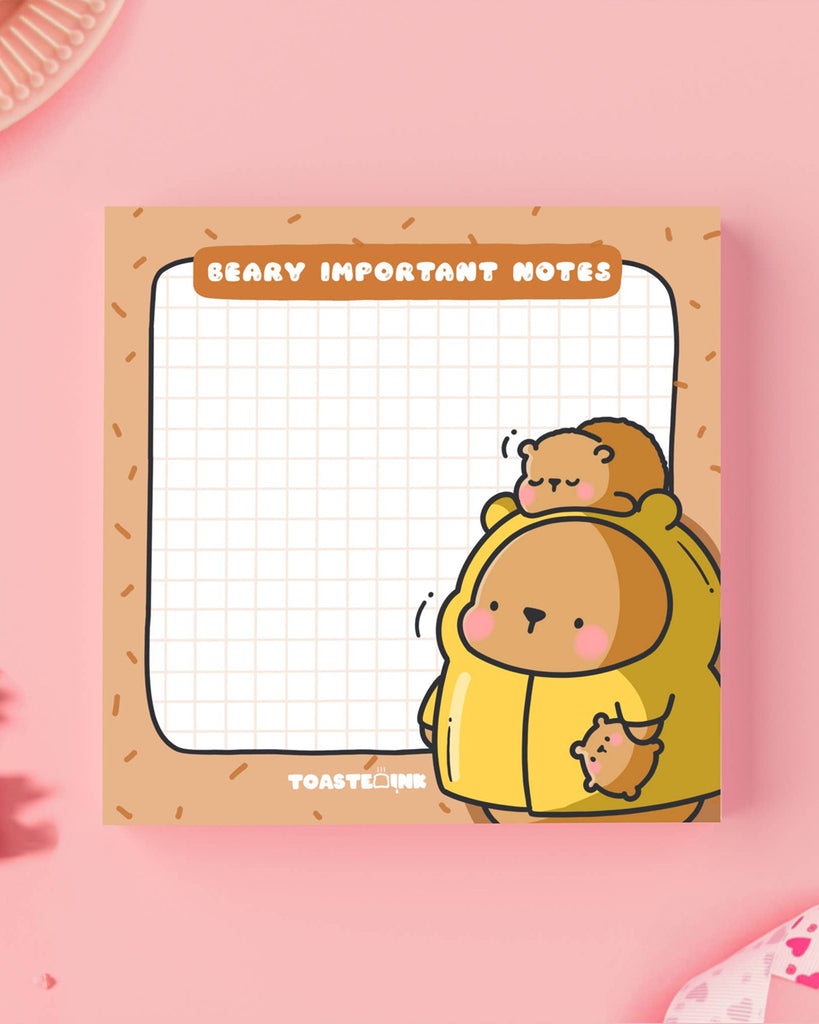 Toastedink’s "Beary Important Notes" sticky pad at Rebel Romance, featuring a cartoon bear family in a cosy design. Photographed flat on a pink surface.
