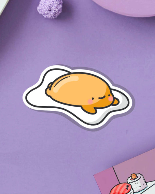 Adorable vinyl sticker of a lazy egg character, lying down with a smile on a purple backdrop. Designed by Toastedink and stocked by Rebel Romance, a UK indie store celebrating quirky, foodie stationery for millennials.