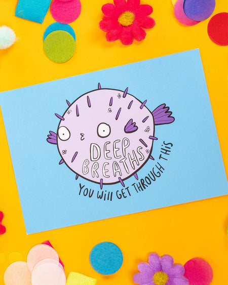 A colourful A6 postcard featuring a round, purple pufferfish on a light blue background with the text “Deep Breaths – You Will Get Through This.” The design is by Katie Abey and aims to promote calm, encouragement, and resilience.