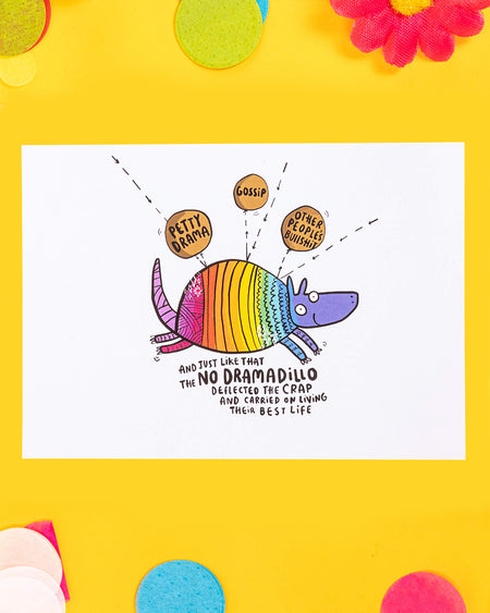 A vibrant A6 postcard featuring a rainbow-coloured armadillo deflecting words like “Petty Drama,” “Gossip,” and “Other People’s Bullsh*t.” The caption reads: “And just like that the No Dramadillo deflected the crap and carried on living their best life.” A fun, empowering illustration by Katie Abey.