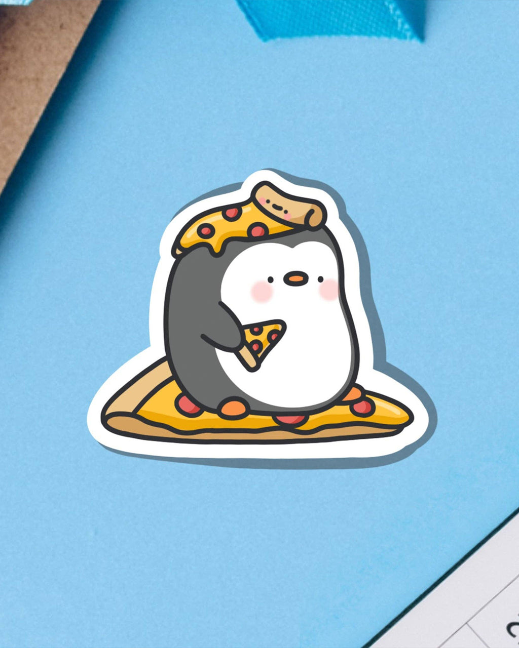 Toastedink's Cute Pizza Penguin Sticker placed on a light blue background. This vinyl sticker features a happy penguin with pizza on its head, in its hand, and under its feet. Perfect for decorating tech, notebooks, or bottles. Sold by Rebel Romance.