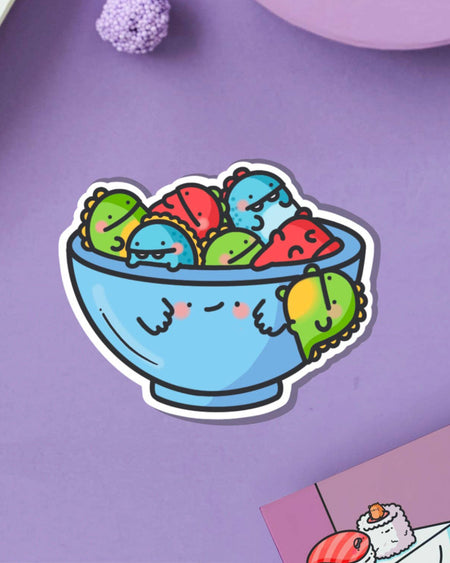 Fun and vibrant Bowl of Dinosaurs sticker from Toastedink, available at Rebel Romance. Shows a happy bowl overflowing with green, red and blue kawaii-style dinos. Perfect for alternative stationery collectors and millennial dino fans.