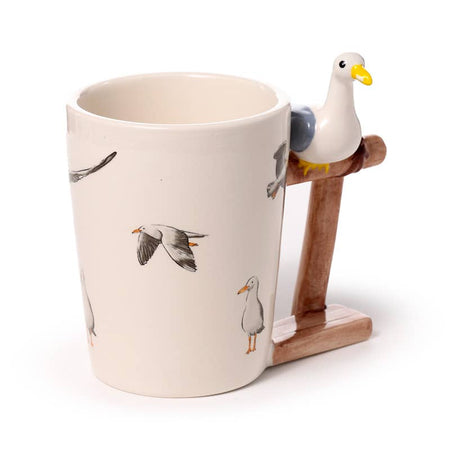 Angled view of the Seagull Buoy Ceramic Mug by Rebel Romance. Decorated with illustrated seagulls in flight and a unique handle shaped like a wooden buoy with a 3D ceramic seagull on top—perfect for coastal vibes and alternative mugs.