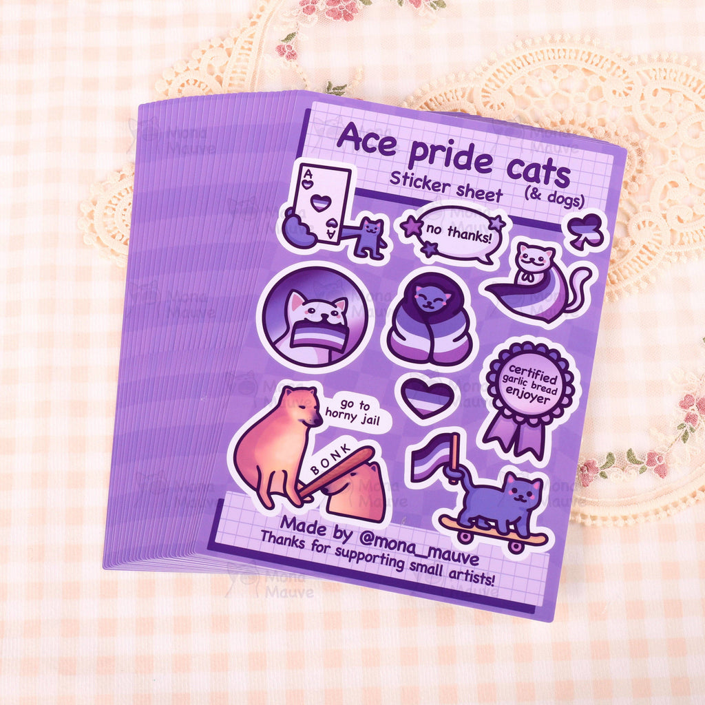 A photo of multiple stacked “Ace pride cats (& dogs)” sticker sheets fanned out on a soft cream gingham fabric background with floral lace. Each purple sheet includes 10 vinyl stickers featuring ace pride-themed cats and dogs, with text like “go to horny jail,” “no thanks!” and “certified garlic bread enjoyer.” Made by @mona_mauve.