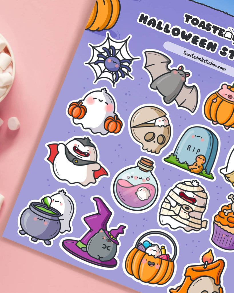 Close-up of Toastedink’s Halloween sticker sheet showing kawaii ghosts, vampire, potion bottle, witch’s cauldron, purple witch hat, and pumpkin trick-or-treat bucket stickers with playful cartoon expressions.