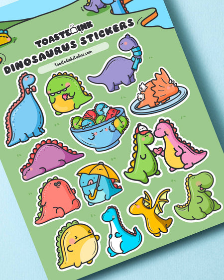 Dinosaurus Sticker Sheet by Toastedink, available from Rebel Romance. Features a variety of cute cartoon dinosaurs including a blue dino with a bowtie, a cereal bowl of dinos, and dino lovebirds. Printed on green background, 5x7 inch sheet.