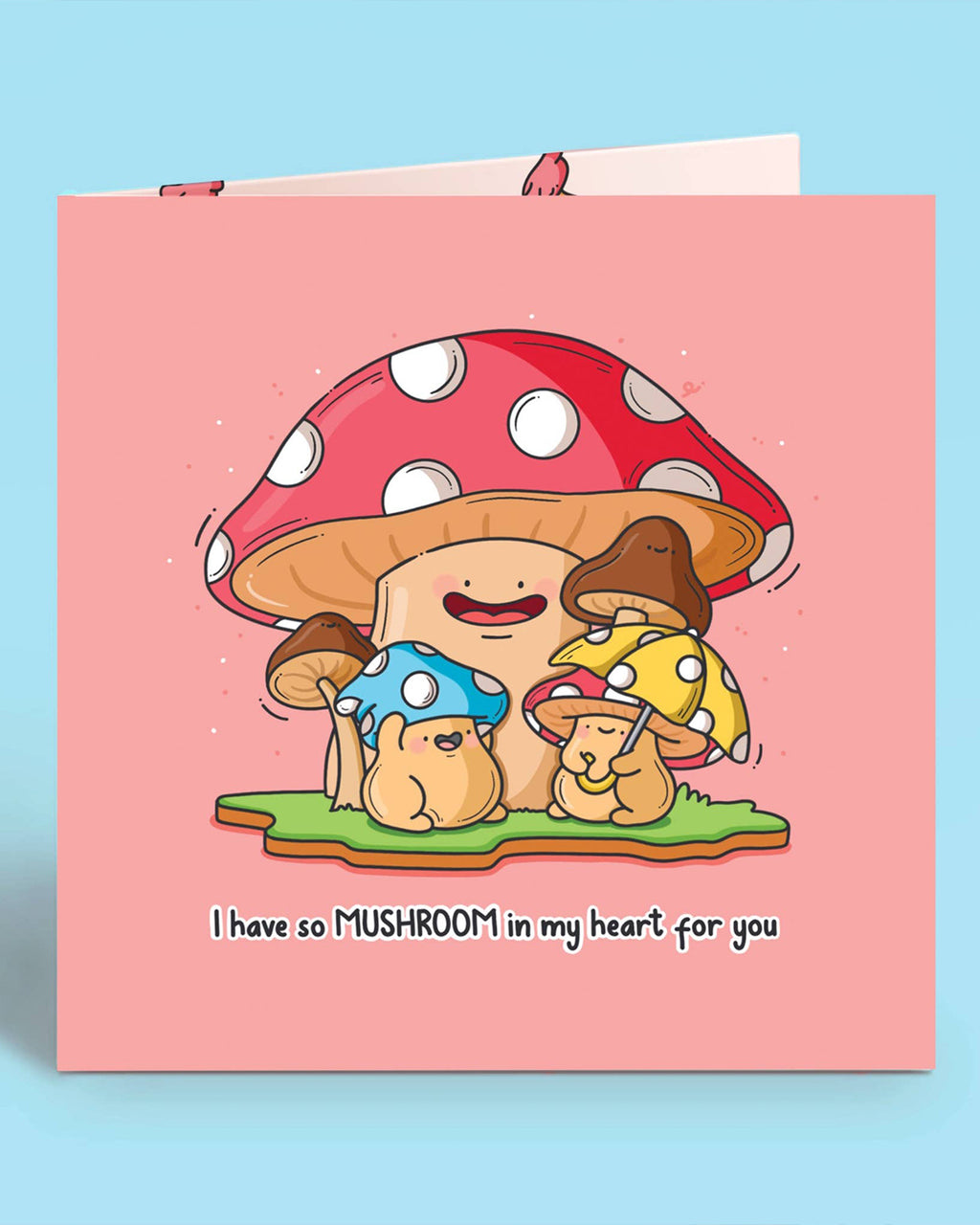 Front view of a pink square greetings card featuring a large happy toadstool surrounded by smaller colourful mushrooms with animal-like faces. Text reads “I have so MUSHROOM in my heart for you.” A cute, pun-filled card designed by Toastedink and available from Rebel Romance in the UK.