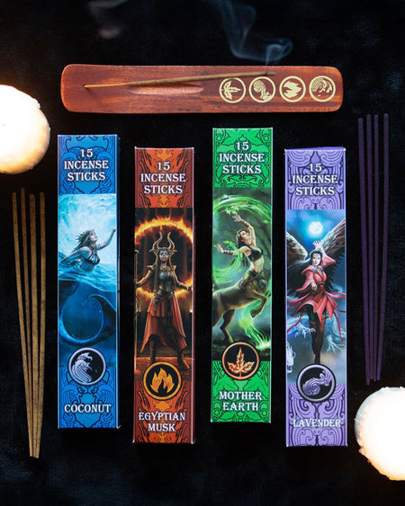 The Elemental Incense Stick Collection laid out on a black background with lit candles, showing incense burning in the wooden holder alongside the four fragrance boxes.