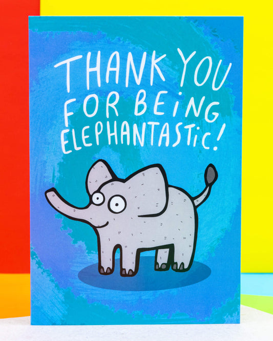 A colourful A6 greeting card by Rebel Romance featuring a cute cartoon elephant with wide eyes and the pun-filled message "Thank you for being elephantastic!" in white lettering. Designed by UK illustrator Katie Abey, this card has a bold blue background and is perfect for spreading positivity and appreciation. Ideal for millennials who love quirky, alternative stationery with uplifting vibes.