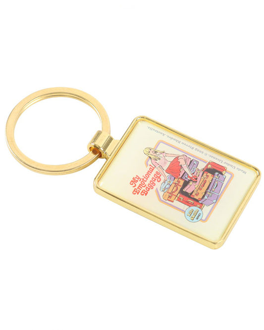 Angled view of the Rebel Romance “My Emotional Baggage” enamel keyring by Steven Rhodes. The gold rectangular keyring shows a retro-style blonde girl sitting on colourful luggage, symbolising carrying feelings in style. A fun, quirky accessory and perfect gift for alternative fashion lovers.