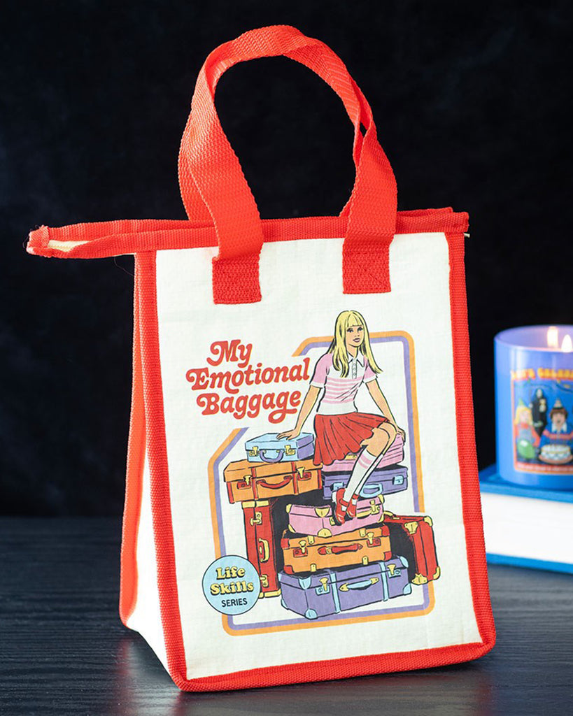 Rebel Romance Steven Rhodes insulated lunch bag "My Emotional Baggage" displayed on a black table beside a retro candle. Cream with red trim and handles, featuring fun vintage-style illustration. A quirky eco-friendly lunch tote made from recycled plastic.