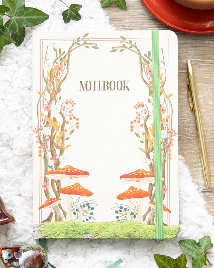 Styled flat lay of the Rebel Romance Enchanted Forest A5 Notebook with a pen, ivy leaves and cosy textures, showing its magical fairytale forest design. A perfect gift for writers, dreamers and note‑takers.