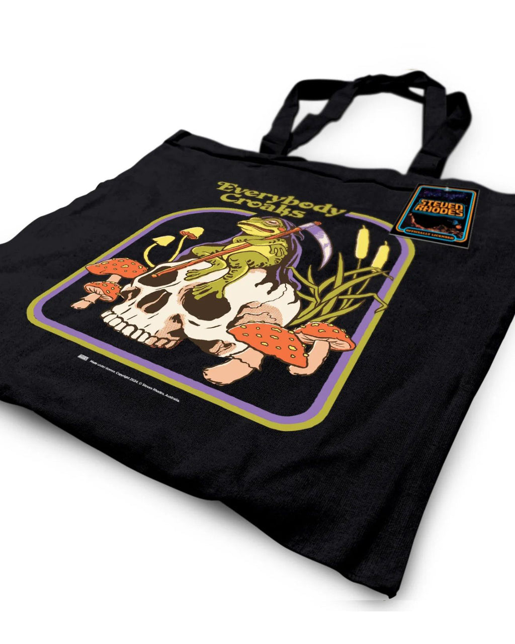 A black tote bag featuring a Steven Rhodes illustration titled “Everybody Croaks.” The design showcases a frog playing a violin while sitting on a skull, surrounded by orange mushrooms and cattails. The text “Everybody Croaks” appears in yellow above the artwork.