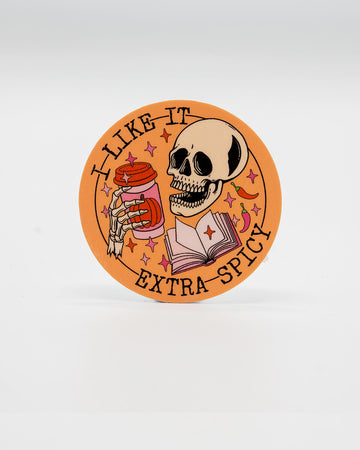 Round die-cut vinyl sticker featuring a grinning skeleton holding a takeaway coffee cup next to an open book, surrounded by sparkles, chillies, and the phrase “I Like It Extra Spicy.” A bold, spooky design perfect for smut readers and lovers of dark humour. Created by Rebel Romance, a small UK brand celebrating alternative style, slow fashion, and cheeky, millennial-friendly bookish gifts.