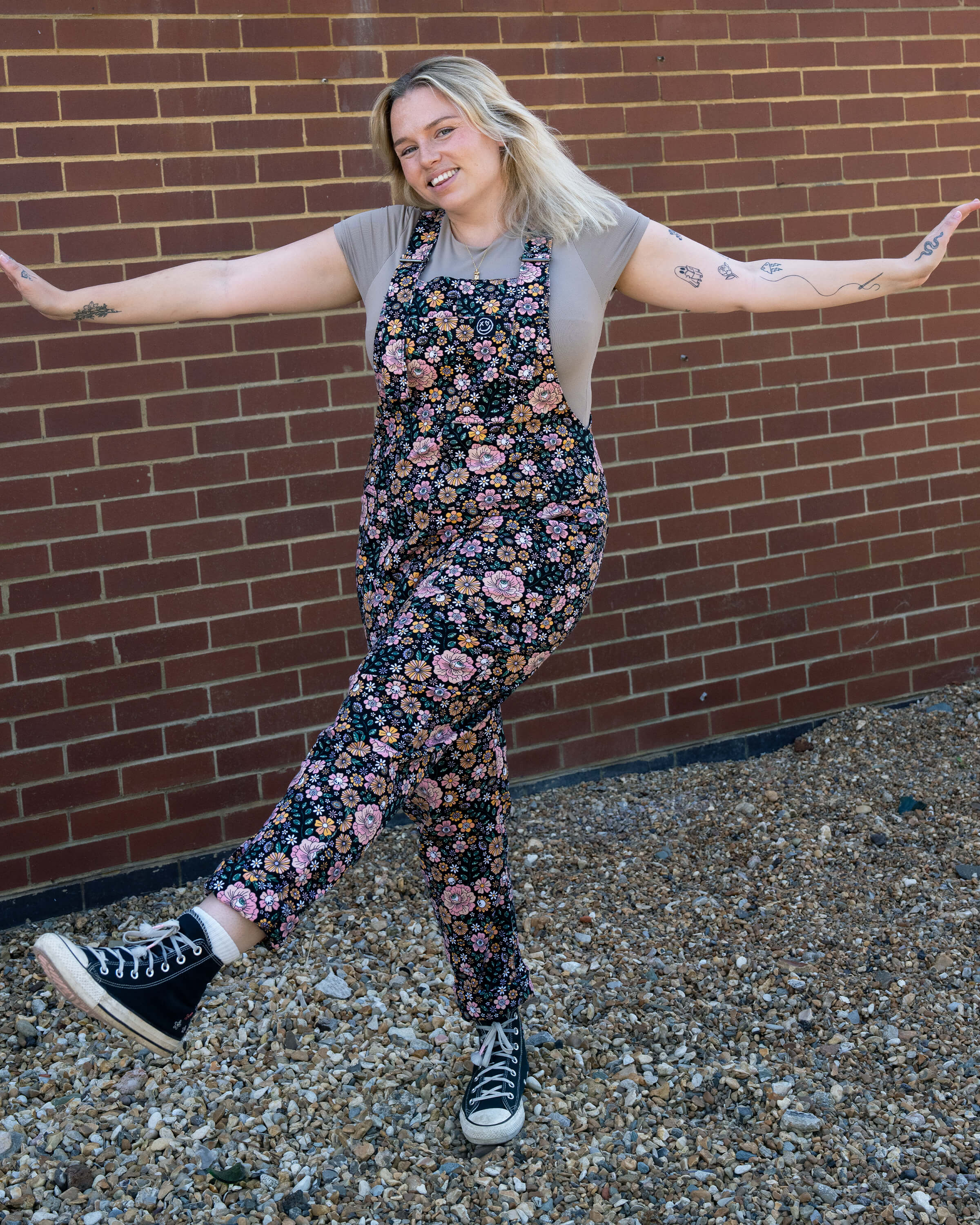 Harleigh dancing in Rebel Romance Eye Spy Floral Stretch Dungarees in floral skull design, styled with Converse trainers and a beige top.
