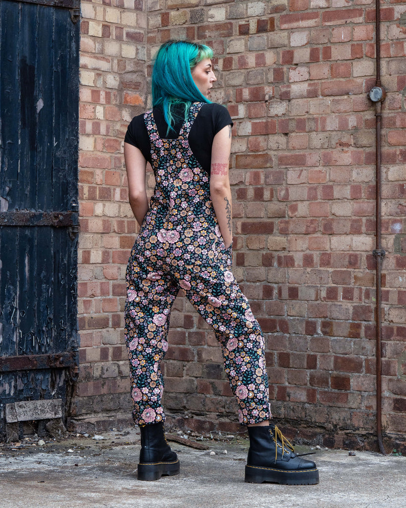 Back view of Claudia in Rebel Romance Eye Spy Floral Stretch Dungarees, showing the floral, skull, and eye pattern on black stretch fabric.