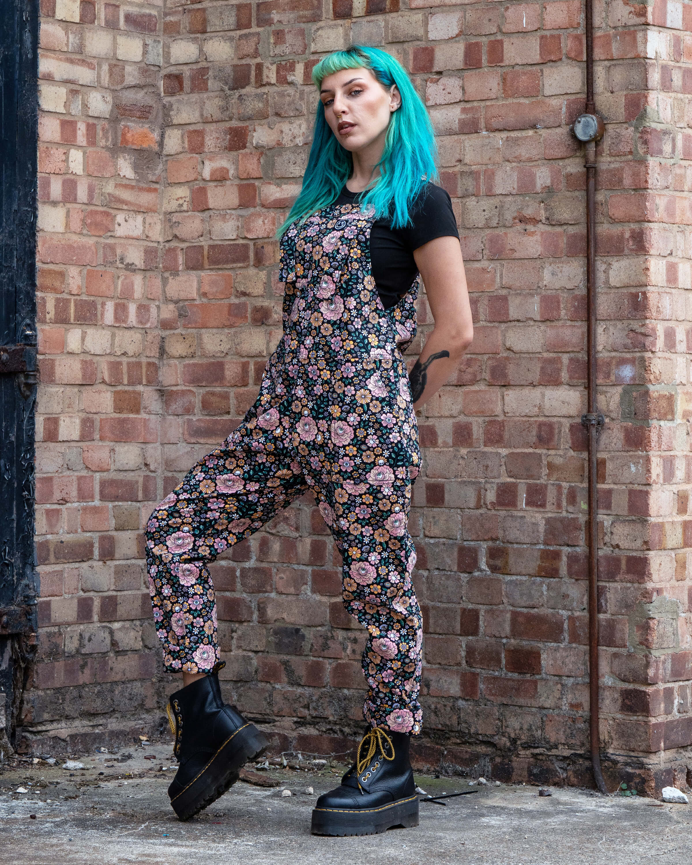 Claudia striking a side pose in Rebel Romance Eye Spy Floral Stretch Dungarees, styled with platform boots and a black t-shirt.