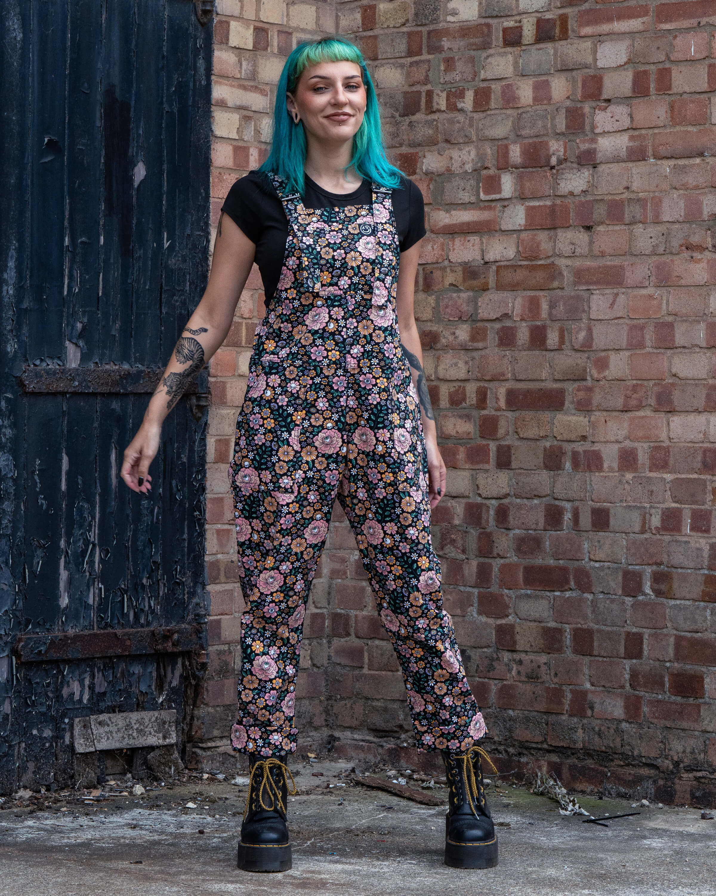 Claudia poses showing the floral printed dungarees styled with a black top.