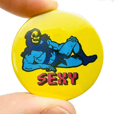 A 38mm button badge featuring Skeletor lounging provocatively on a bright yellow background with the word “SEXY” written in bold pink retro-style letters. This high-gloss pin is a cheeky nod to pop culture, perfect for personalising your accessories. Designed by Bite Your Granny.