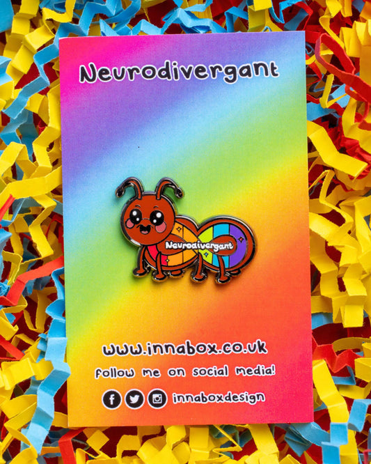 A colourful enamel pin from Rebel Romance featuring a cute cartoon ant with a rainbow neurodivergent flag design and the word "Neurodivergant" across its body. The pin is displayed on a rainbow gradient backing card surrounded by red, yellow, and blue shredded paper. Designed by Innabox, a UK-based brand championing mental health awareness and alternative style.