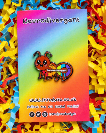 A colourful enamel pin from Rebel Romance featuring a cute cartoon ant with a rainbow neurodivergent flag design and the word "Neurodivergant" across its body. The pin is displayed on a rainbow gradient backing card surrounded by red, yellow, and blue shredded paper. Designed by Innabox, a UK-based brand championing mental health awareness and alternative style.