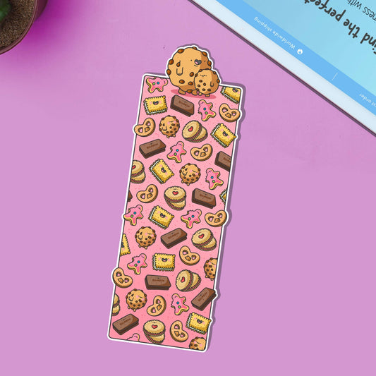 Glossy biscuit-themed bookmark featuring cartoon illustrations of cookies, pink iced biscuits, bourbons, jammy dodgers and other treats on a pink background. Topped with two cute chocolate chip cookies.
