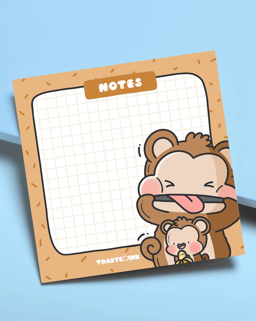Toastedink monkey sticky note pad shown on a pale blue background. The design includes adorable cartoon monkeys with blush cheeks and grid paper. Stocked by Rebel Romance, a small UK biz curating joyful and unique accessories.