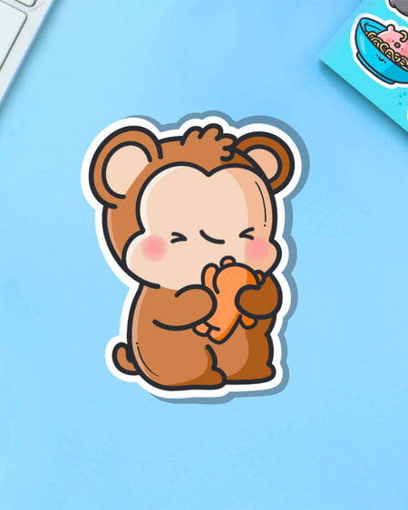 Kawaii-style monkey cuddling a teddy bear sticker, printed on glossy vinyl. Displayed on a light blue surface with Rebel Romance branding. Perfect for laptops, bottles, and more. Designed by Toastedink, stocked by Rebel Romance.