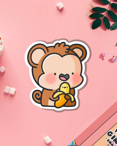 Cute monkey vinyl sticker holding a smiling banana, surrounded by marshmallows and florals on a pink background. Stocked by Rebel Romance, a UK brand celebrating alternative style and quirky characters. Designed by Toastedink.