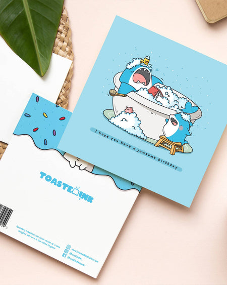 Toastedink “Jawsome Birthday” card shown with back design. Features a large shark in a tub surrounded by bubbles, a duck, and a smaller shark. Stocked by Rebel Romance. A cute and quirky square birthday card printed in the UK.