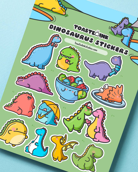 Toastedink dinosaur sticker sheet showing fun illustrations like umbrella dinos, dinos with wings, and dino partners. Professionally printed in the UK and sold by Rebel Romance. 5x7 inch sticker sheet on green background.