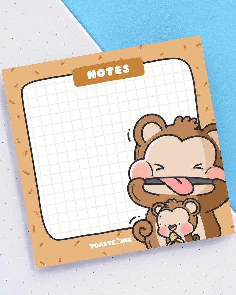 Playful Toastedink monkey sticky note pad photographed on a slanted angle. Features grid paper and a pair of cute monkeys hugging a banana. Part of Rebel Romance’s alternative and fun stationery collection in the UK.