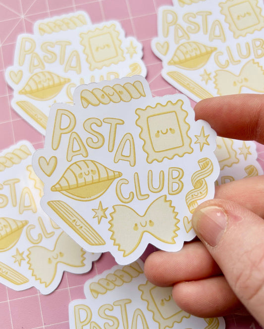 A close-up image of a hand holding one "Pasta Club" glossy sticker from Rebel Romance, surrounded by more of the same sticker design in the background. Features adorable illustrated pasta shapes in yellow tones, ideal for showing off your love of carbs.