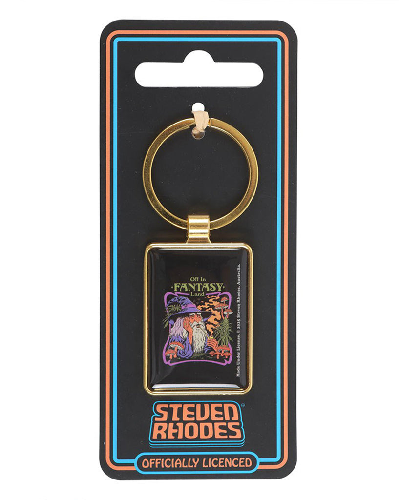 Steven Rhodes Fantasy Land keyring from Rebel Romance displayed on branded packaging. Black backing card with retro orange and blue border and the Steven Rhodes logo. The gold-framed enamel design shows a wizard smoking a pipe, surrounded by mushrooms and fantasy plants with the text “Off in Fantasy Land.”